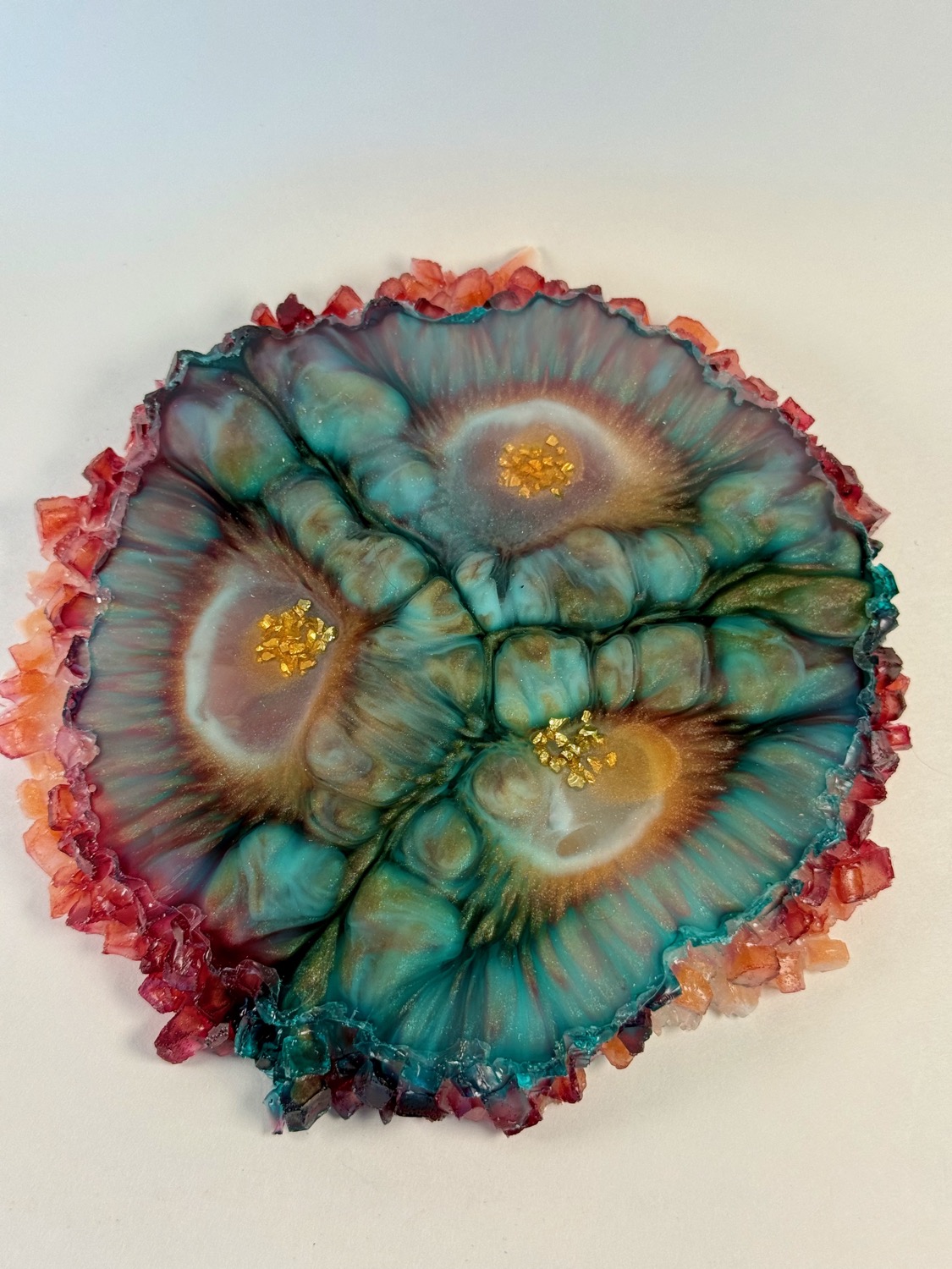 Teal and rust bull's-eye resin coaster with red crystal edges and gold flakes