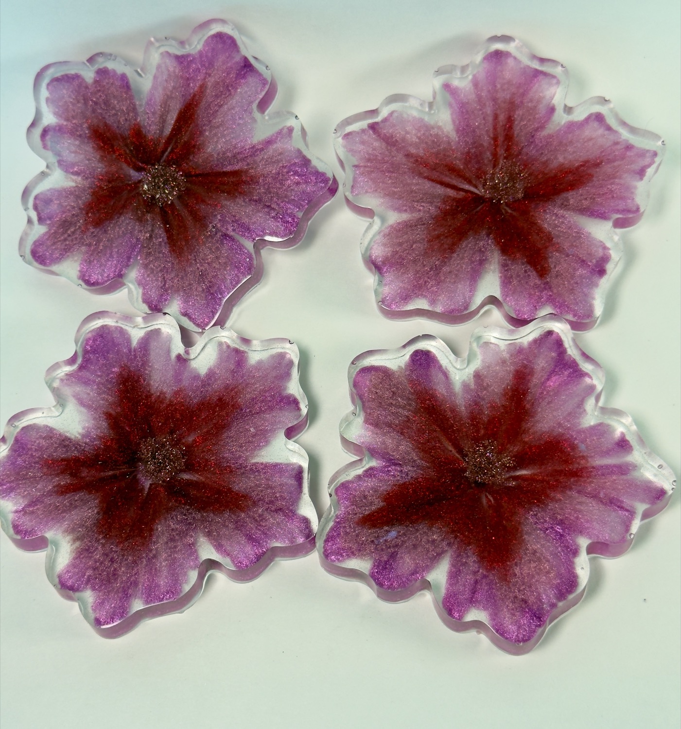 Set of 4 flower-shaped resin coasters with purple and magenta glitter petals and clear scalloped edges